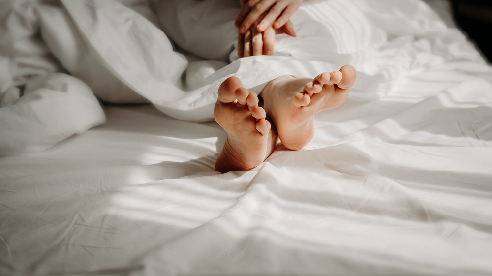 Woman is lying with bare feet in bed, sleeping under white cosy duvet