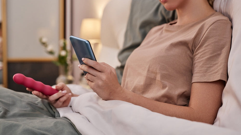 Women holding sex toy in bed