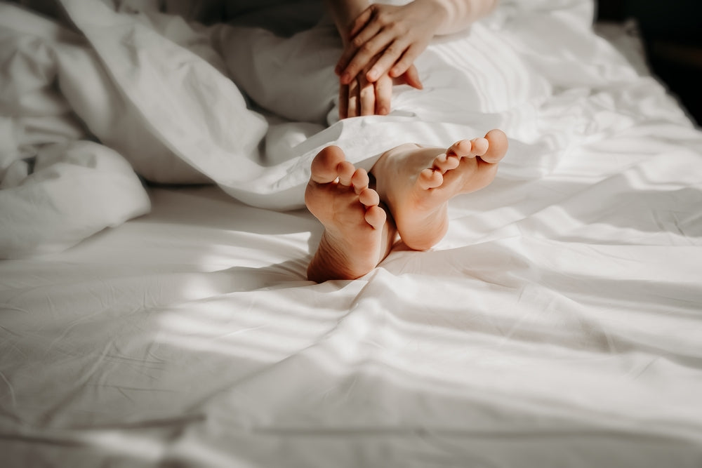 Woman is lying with bare feet in bed, sleeping under white cosy duvet